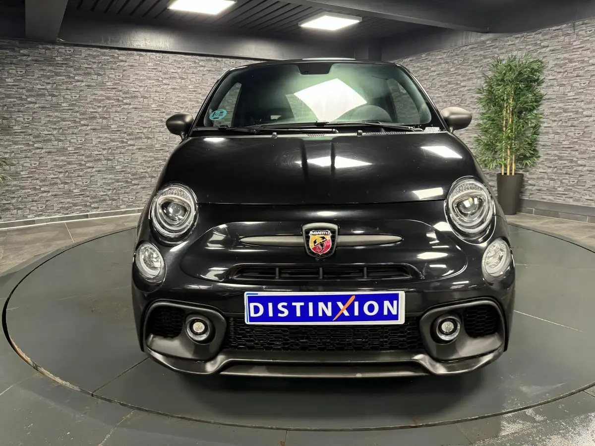 Vue avant d'une ABARTH 595 Competizione noire métallisée avec logo Abarth et phares ronds LED dans un showroom.