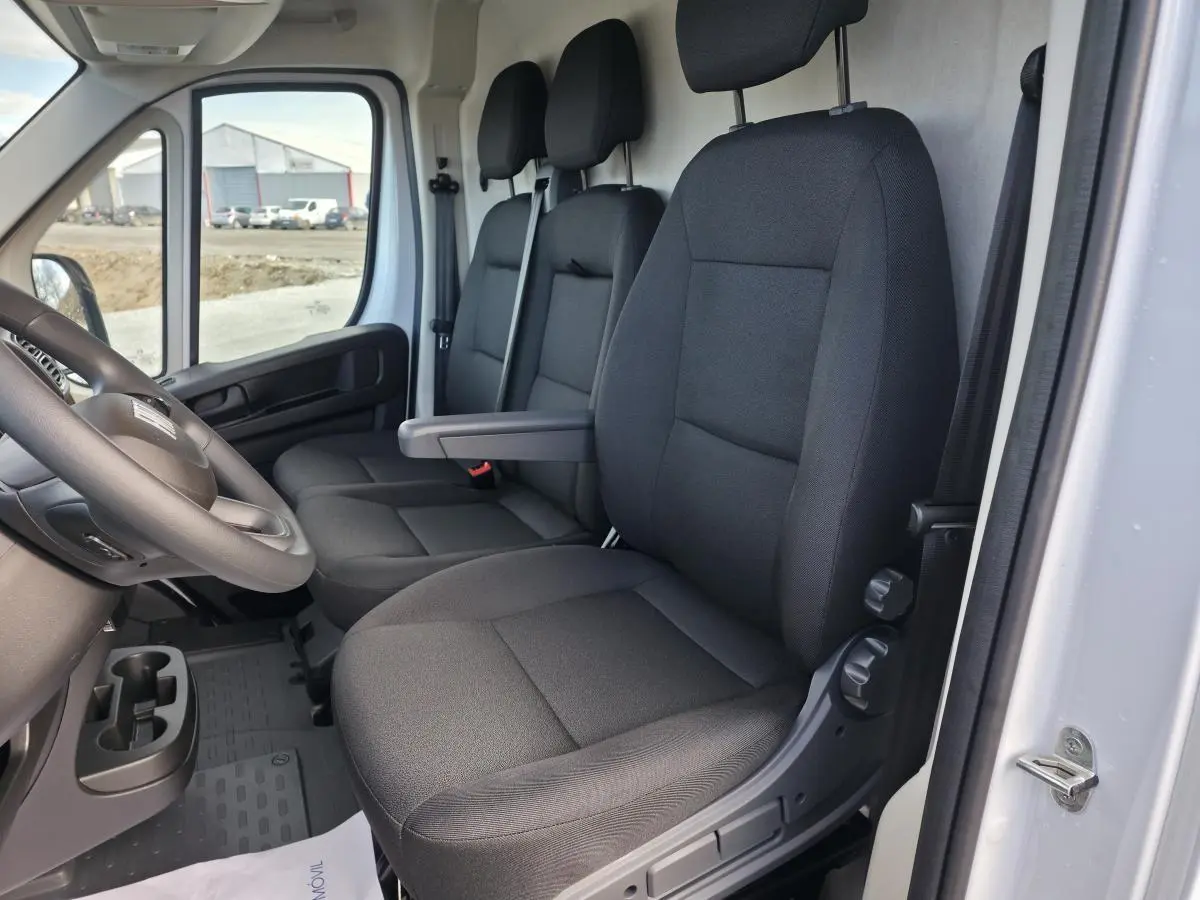 Vue intérieure côté conducteur du Fiat Ducato Fourgon blanc, montrant les sièges en tissu noir et le volant.