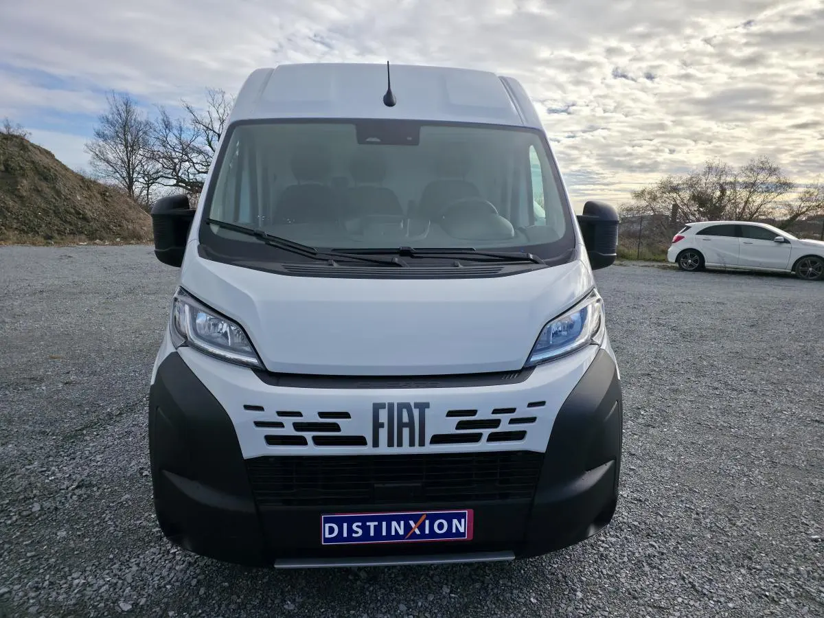 Vue de face du fourgon FIAT Ducato blanc avec pare-chocs noir et logo FIAT bien visible sur un parking extérieur.