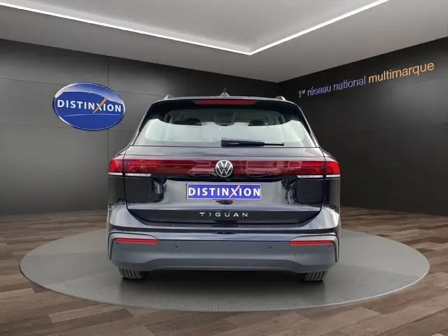 Vue arrière d'un Volkswagen Tiguan noir 2024, avec feux arrière allongés et logo distinctif sur un fond showroom.