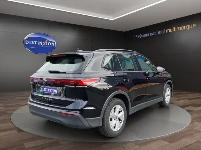 Volkswagen Tiguan noir 2024 vu en 3/4 arrière droit dans un showroom avec feux arrière LED allumés.