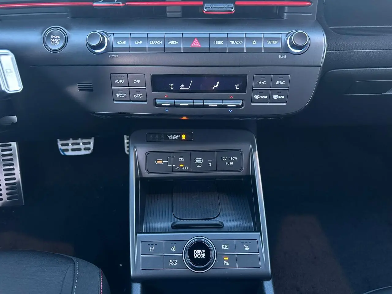 Vue centrée sur la console centrale du Hyundai KONA noir, avec commandes climatisation, chargeur sans fil et bouton Drive Mode.