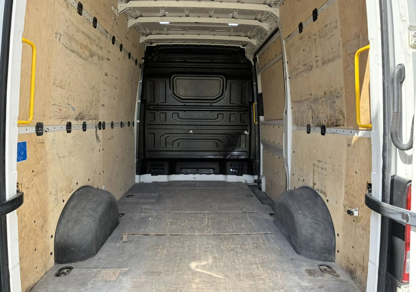 Vue intérieure arrière du fourgon Volkswagen Crafter blanc, montrant l’espace de chargement avec parois en bois et plancher caoutchouc.