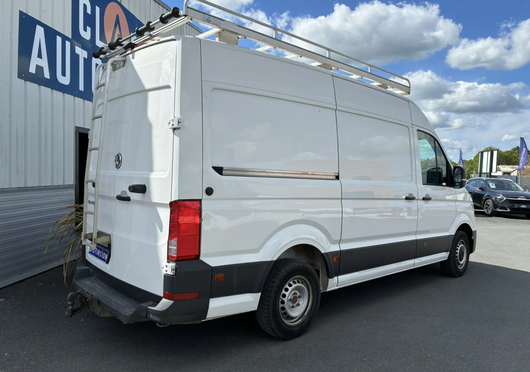 Vue 3/4 arrière droite d'un Volkswagen Crafter blanc avec galerie de toit et échelle métallique arrière.