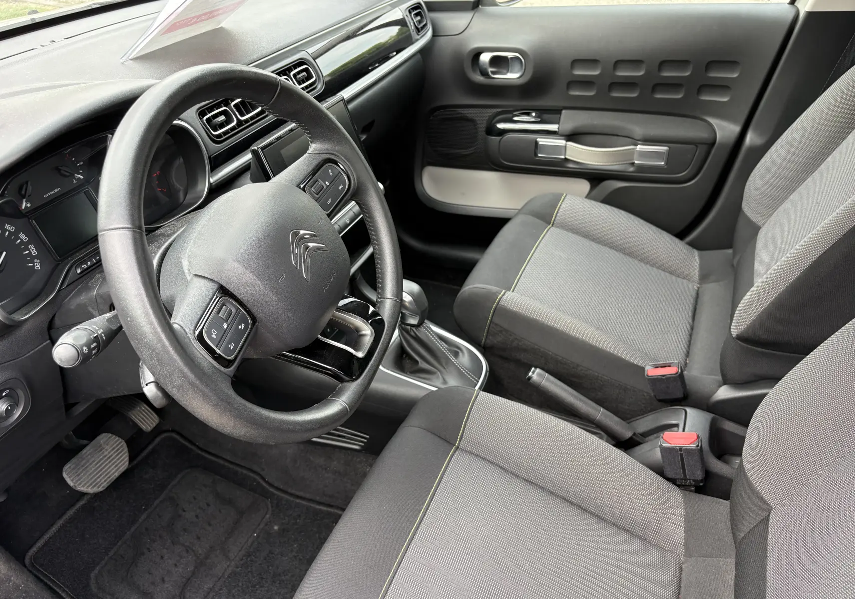 Intérieur beige de Citroën C3 2019 vu côté conducteur, volant multifonction et sièges tissu gris avec surpiqûres jaunes.