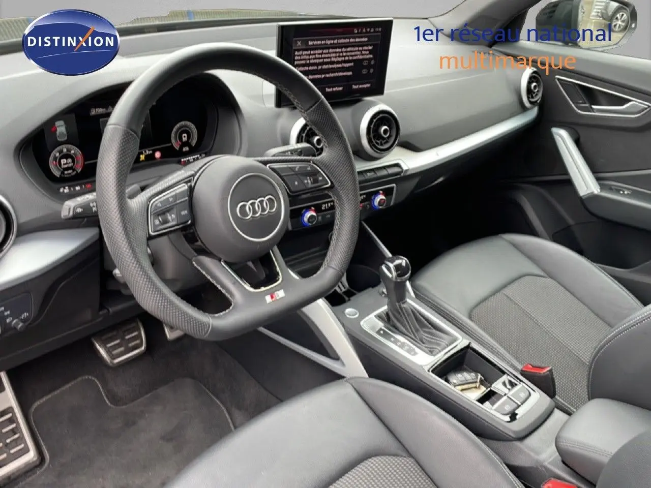 Vue intérieure de l'Audi Q2 35 2.0 TDI S-Line 2025, mettant en valeur le volant cuir perforé et la console centrale moderne.