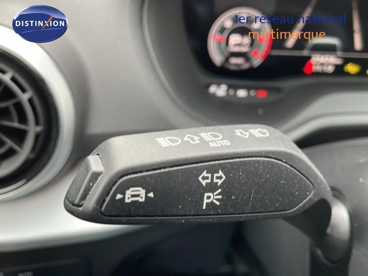 Gros plan sur la commande de clignotant et feux d'un Audi Q2 noir mito metal, intérieur avec tableau de bord flou en arrière-plan.