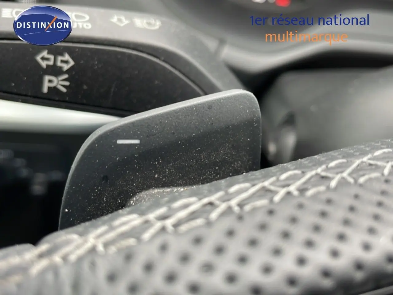 Gros plan sur la palette de changement de vitesse derrière le volant en cuir perforé de l'Audi Q2 noir mito metal.