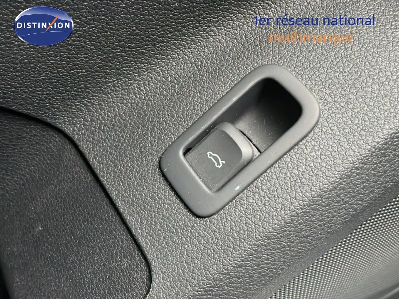 Gros plan sur le bouton d'ouverture de coffre intégré dans le revêtement noir texturé intérieur de l'Audi Q2 2025.