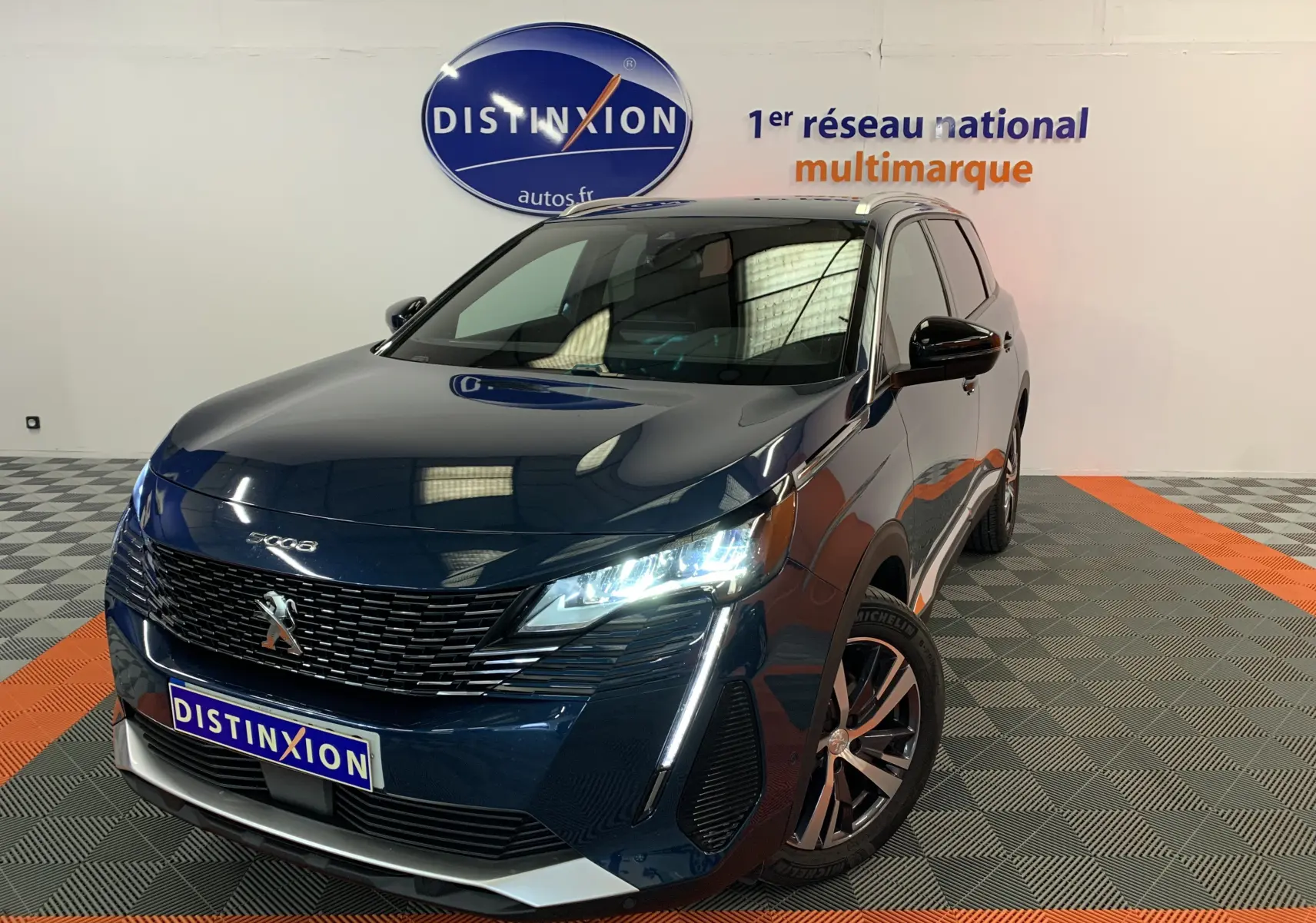 Peugeot 5008 bleu Célèbes en 3/4 avant droit, phares LED allumés, calandre noire et jantes alliage visibles.
