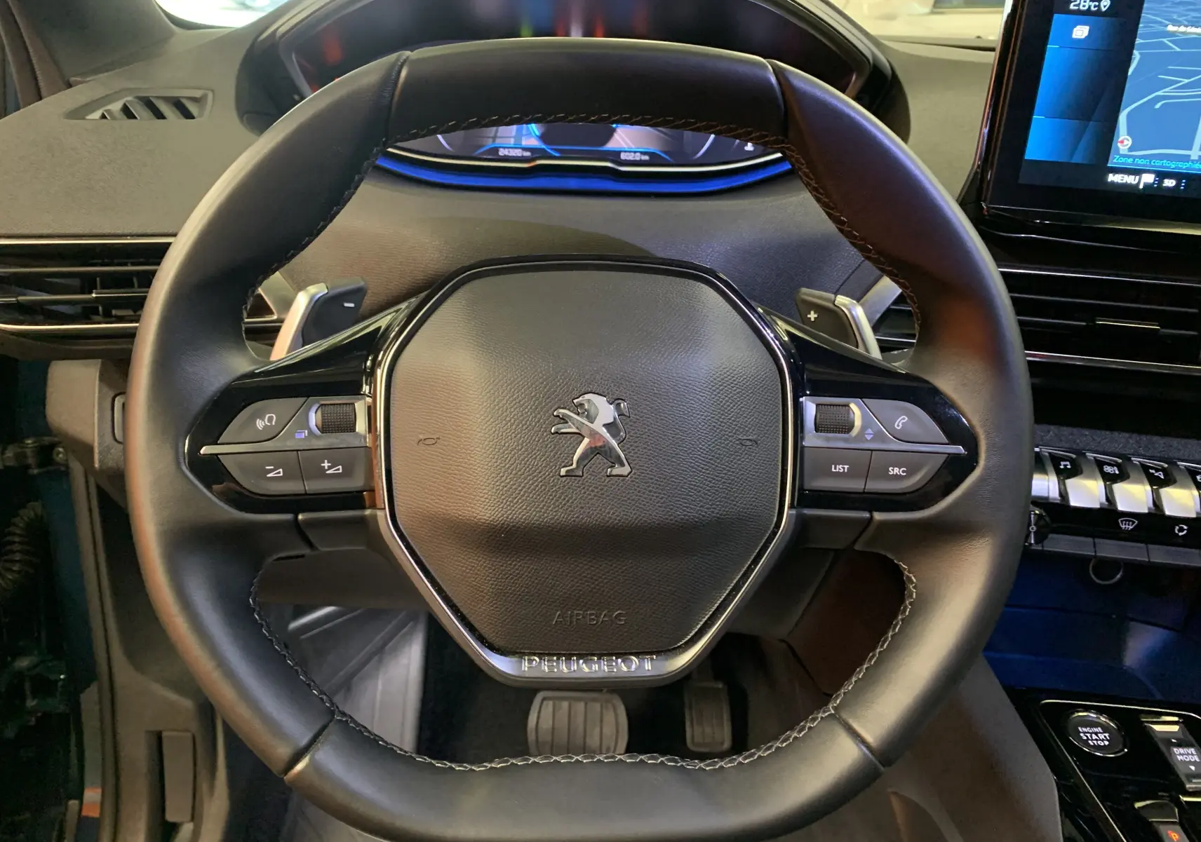 Vue rapprochée du volant cuir noir du Peugeot 5008 2024 avec commandes intégrées et tableau de bord numérique.