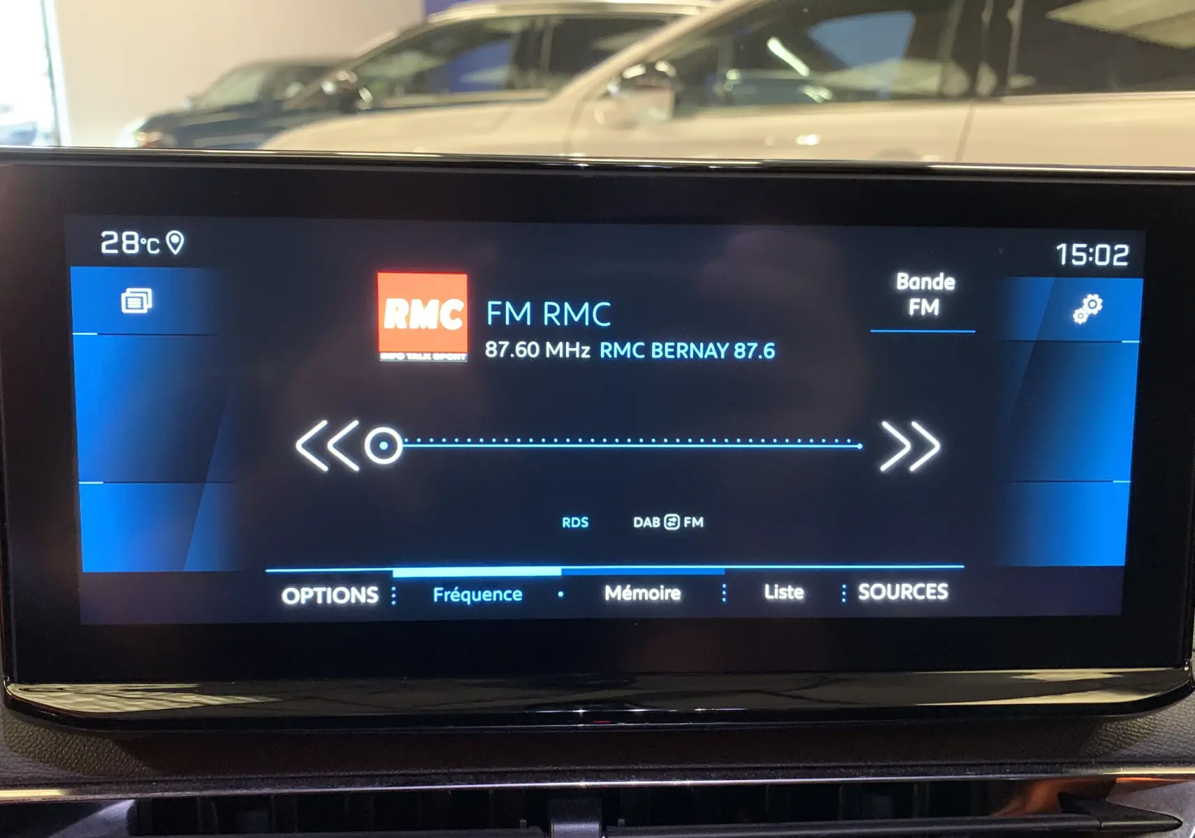 Écran tactile central du Peugeot 5008 II Ph.2 Bleu Célèbes affichant la radio FM RMC à 87,6 MHz en intérieur.