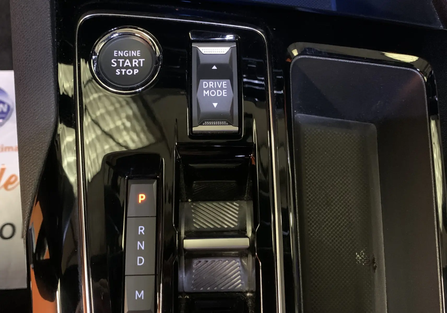 Gros plan sur la console centrale noire brillante du Peugeot 5008 Bleu Célèbes, avec bouton start/stop et sélecteur de mode de conduite.