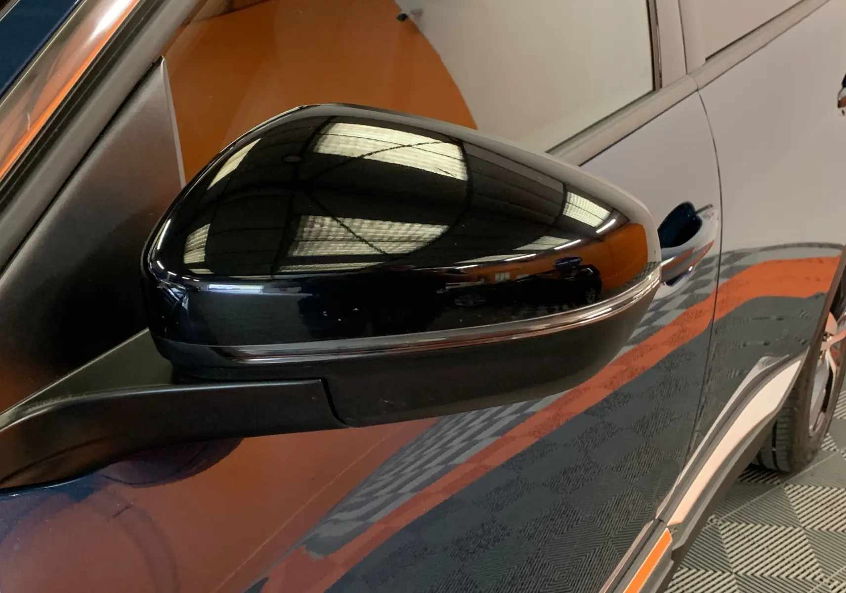 Rétroviseur noir brillant côté gauche du Peugeot 5008 bleu Célèbes, vue rapprochée sur la portière avant.