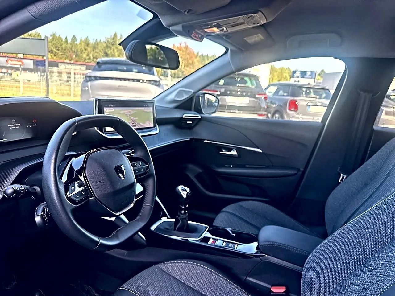 Intérieur de la Peugeot 208 1.2 100 allure noir, vue côté conducteur, volant compact et écran tactile central visible.