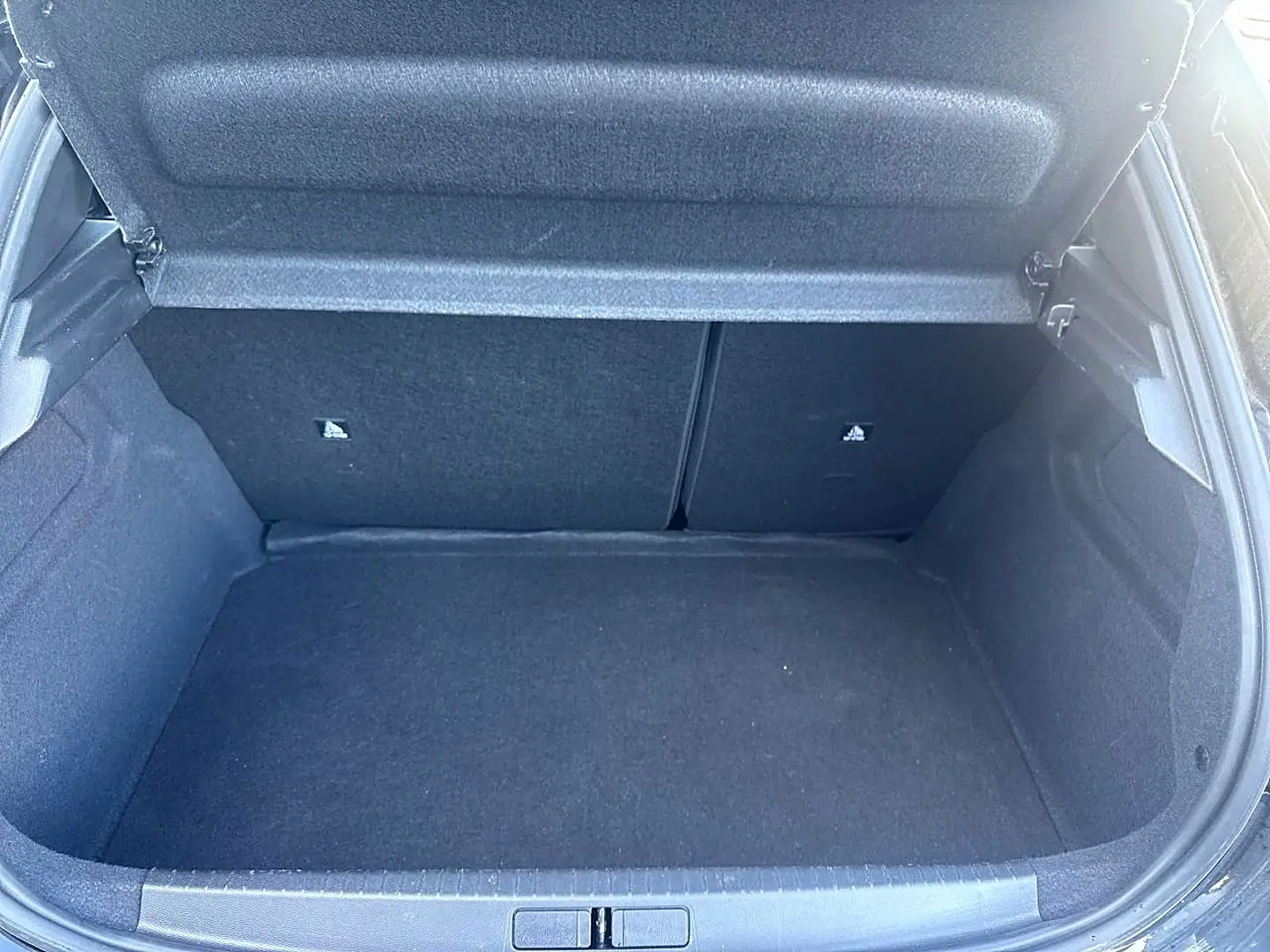 Coffre ouvert vu de face d’une Peugeot 208 noire, montrant l’espace de chargement vide et la tablette cache-bagages relevée.