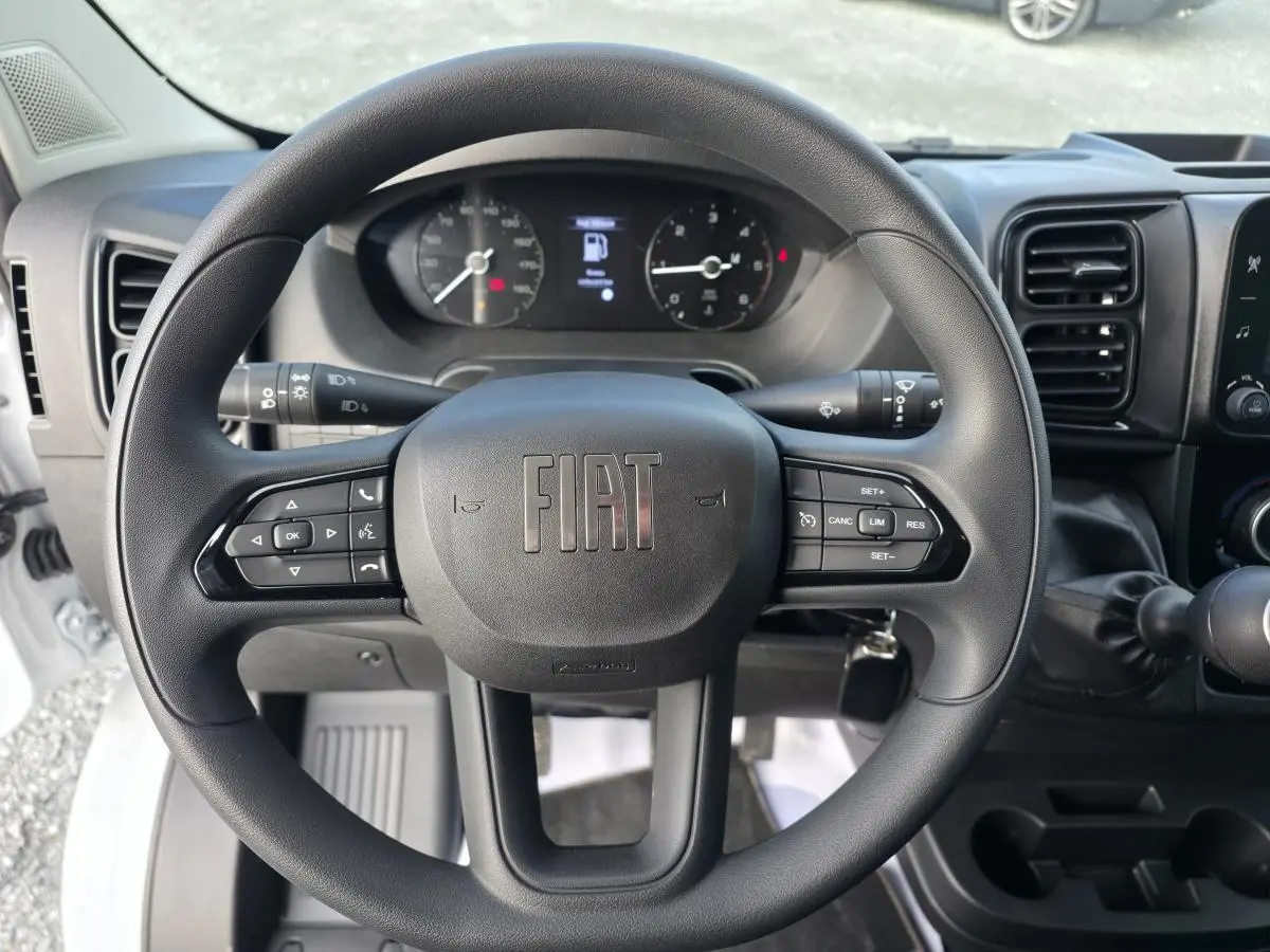 Vue intérieure du tableau de bord et volant noir du Fiat Ducato Fourgon blanc, avec commandes au volant et ventilation centrale.