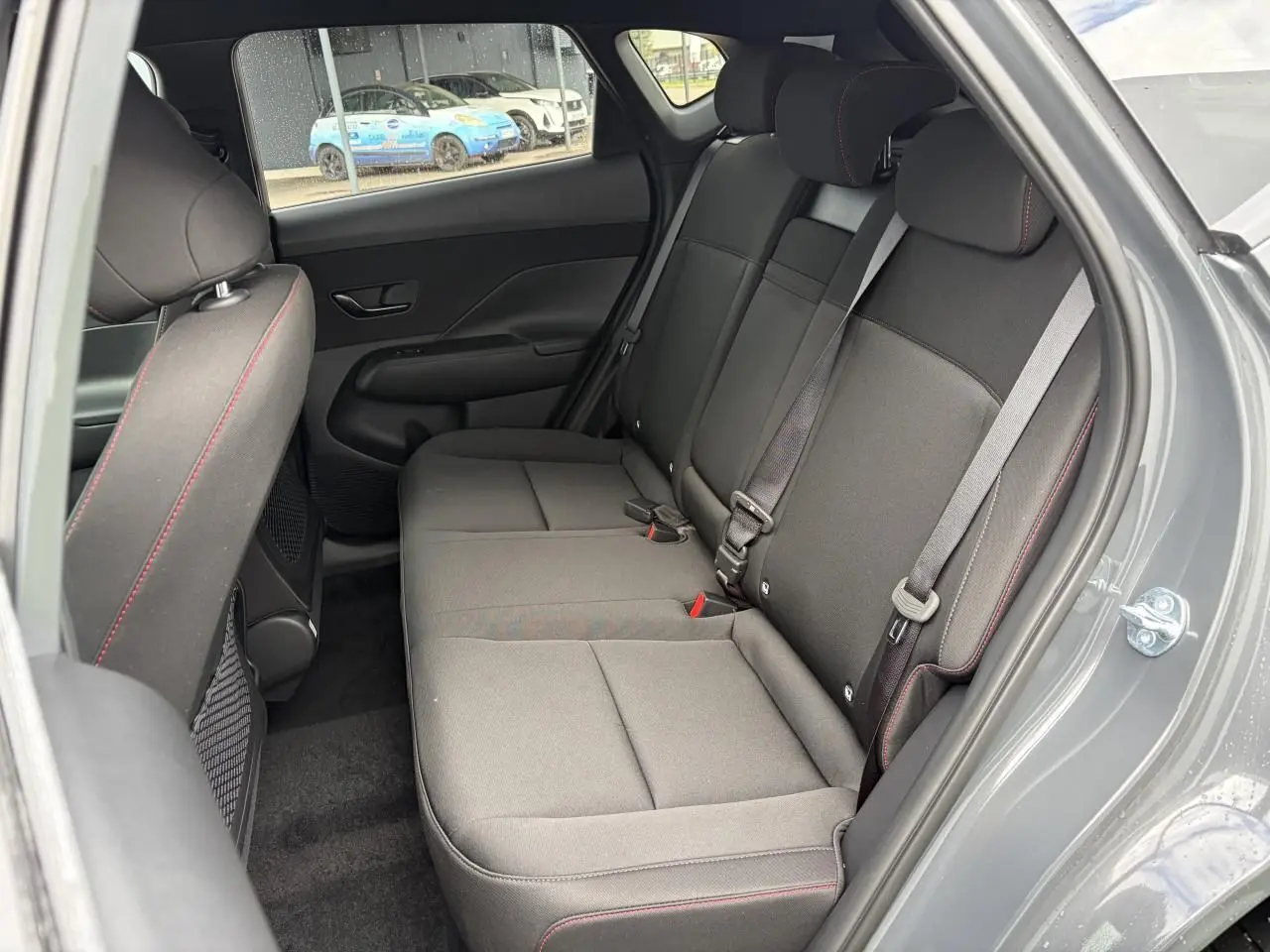 Vue intérieure côté droit sur la banquette arrière noire avec surpiqûres rouges du Hyundai KONA II Ecotronic Grey.