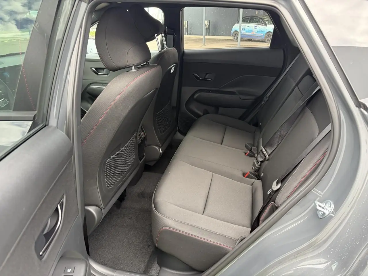 Vue côté droit de l’habitacle arrière du Hyundai KONA 2026 gris Ecotronic, sièges tissu avec surpiqûres rouges.