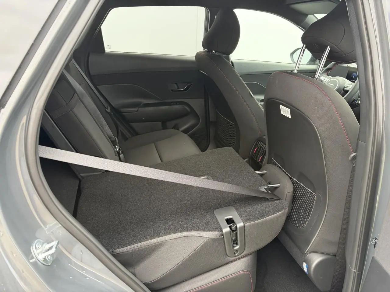 Vue intérieure côté gauche arrière du Hyundai KONA 2026 gris Ecotronic, siège rabattable et ceinture visible.