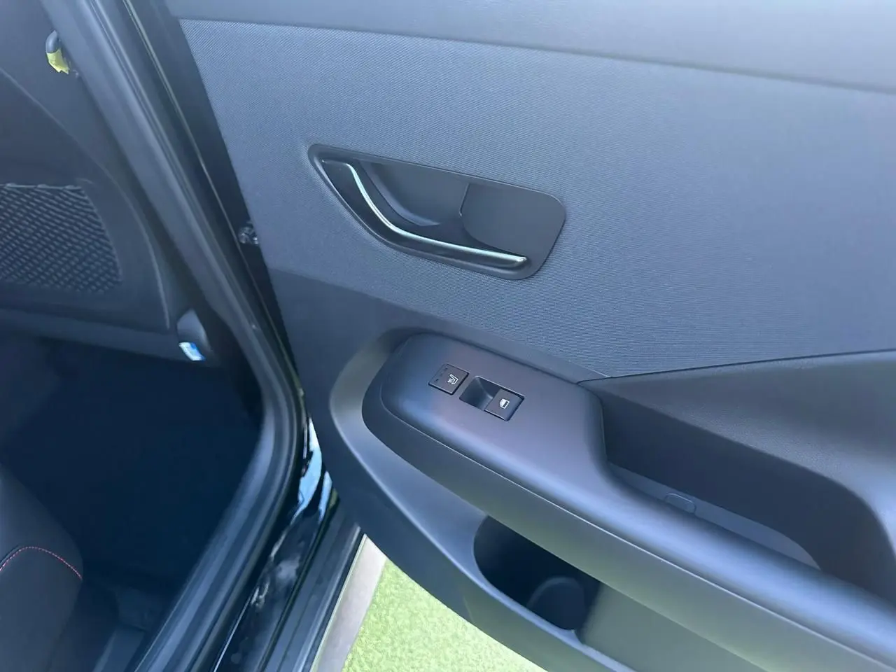 Vue intérieure côté gauche de la porte arrière d'une Hyundai Kona II grise, avec commandes de fenêtre et poignée noire.