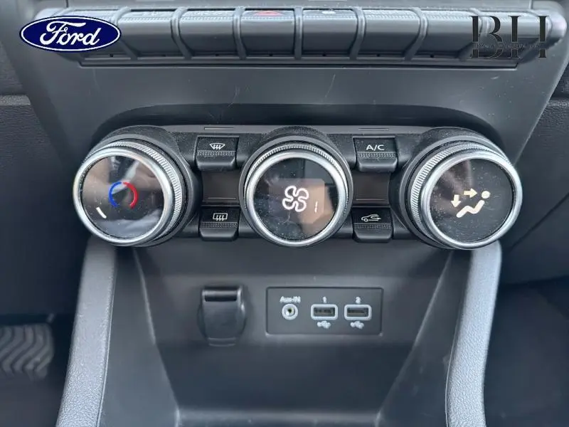 Gros plan sur les commandes de climatisation et les ports USB d’un tableau de bord noir, intérieur d’une voiture non identifié.