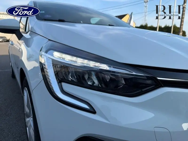 Gros plan sur le phare avant gauche blanc de la Renault Clio 1.6 E-Tech 2021 avec feux LED et carrosserie blanche glacée.