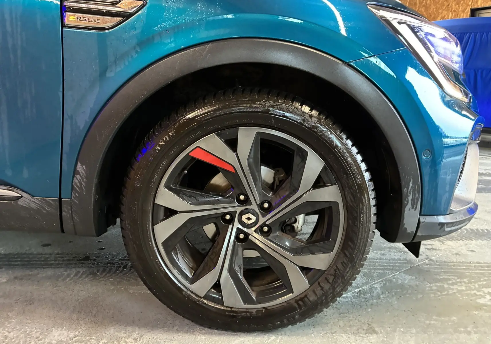 Gros plan sur la roue avant droite d’un Renault Arkana bleu 1.3 TCE 140 RS-LINE avec jante alu bicolore et logo Renault.