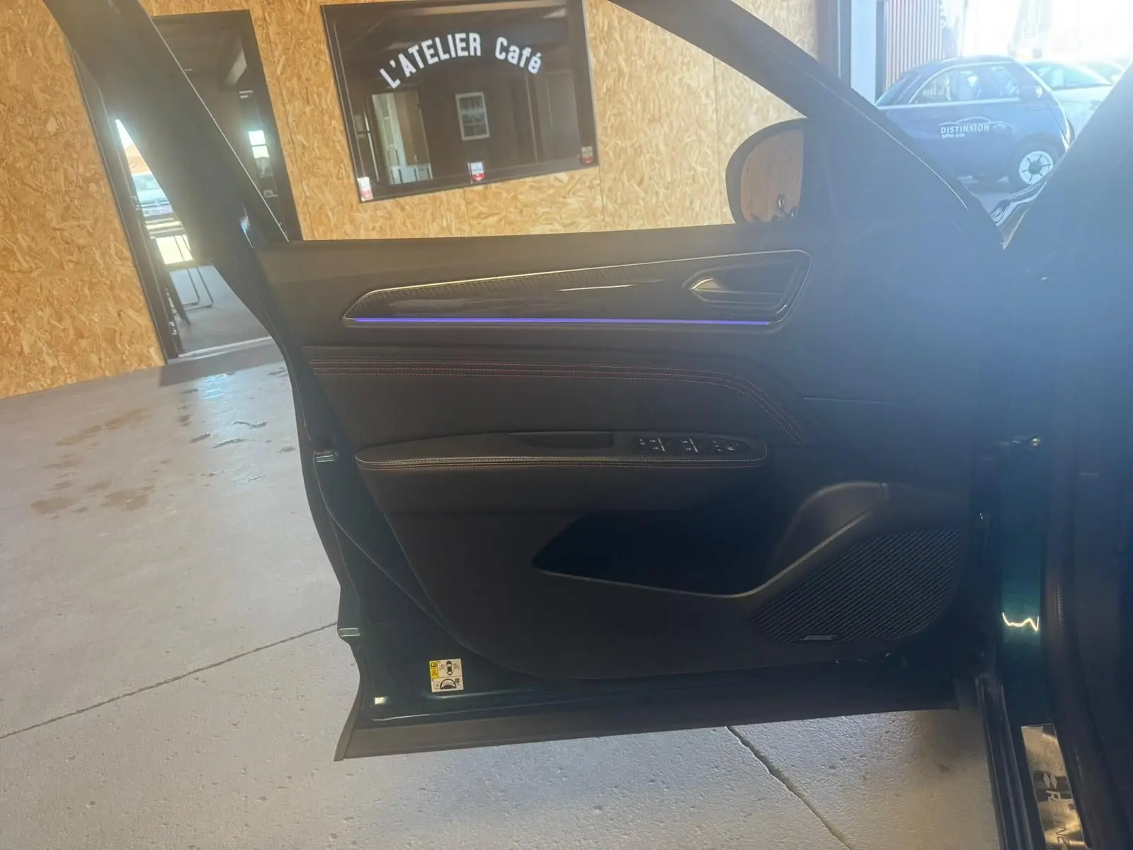 Vue intérieure de la porte avant gauche ouverte d’un Renault Arkana bleu, avec commandes électriques et éclairage d’ambiance bleu.