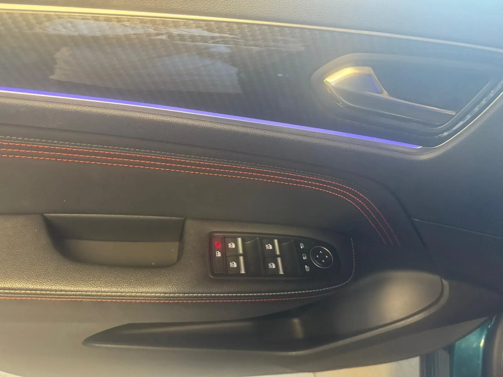 Gros plan sur la porte côté conducteur du Renault Arkana bleu, avec surpiqûres rouges et commandes de vitres.