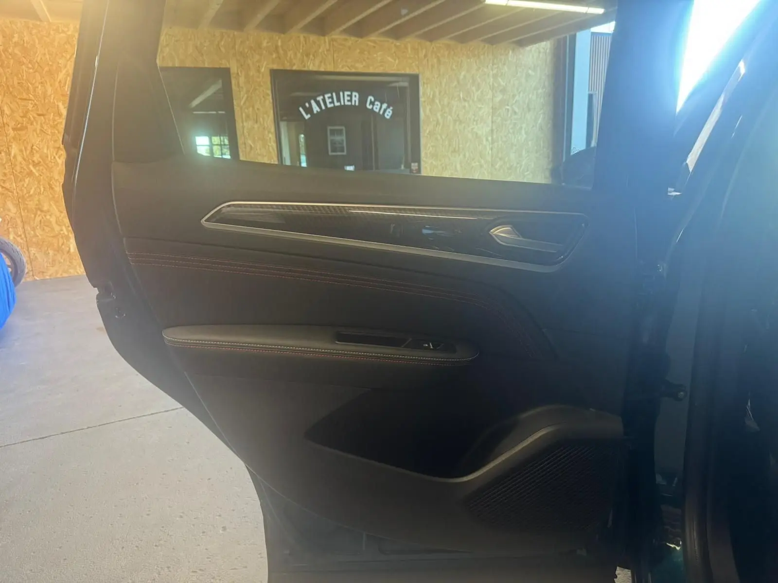 Vue intérieure de la porte arrière droite du Renault Arkana bleu, avec garniture noire et surpiqûres rouges visibles.
