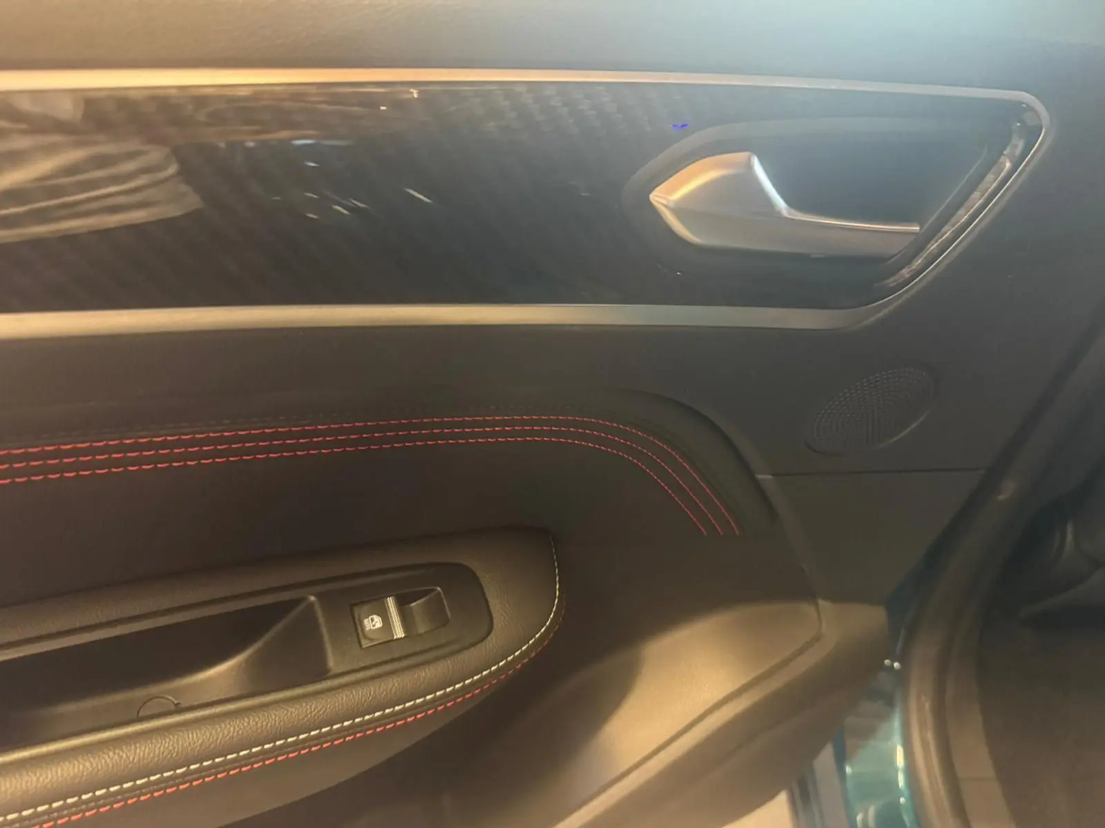 Détail de la porte intérieure côté gauche du Renault Arkana bleu, avec surpiqûres rouges et poignée argentée.