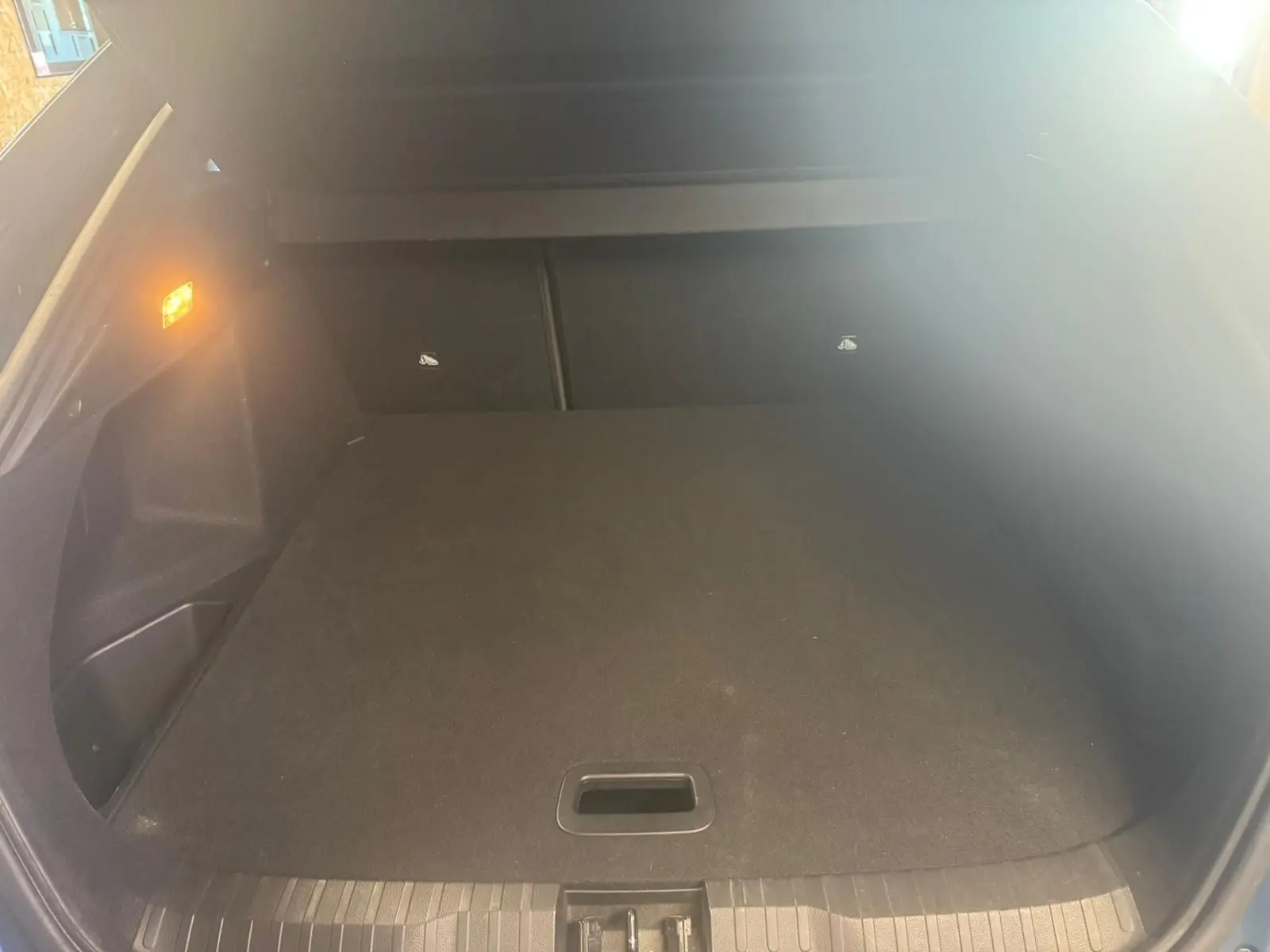 Coffre ouvert vu de l'arrière d'un Renault Arkana bleu, espace de chargement propre et éclairage latéral allumé.