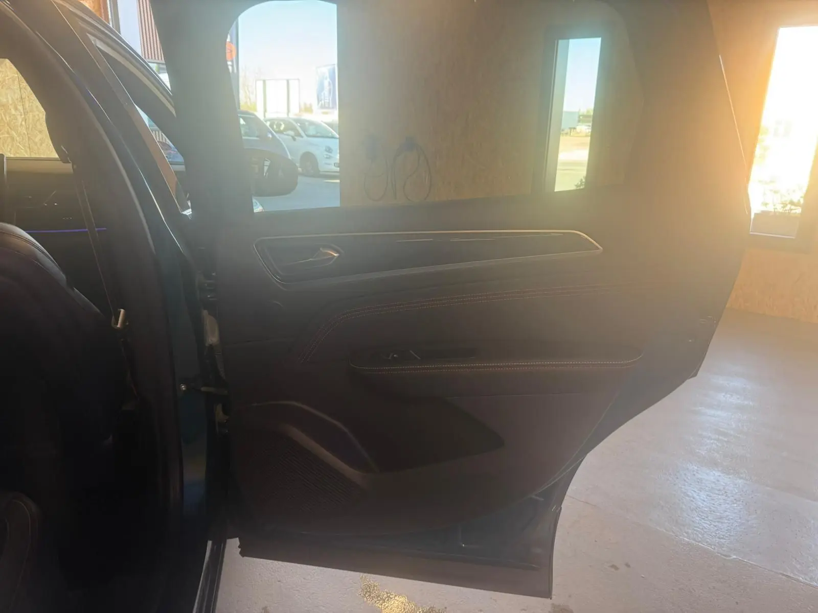 Vue intérieure de la porte arrière gauche d'un Renault Arkana bleu, avec détails en cuir noir et surpiqûres rouges.