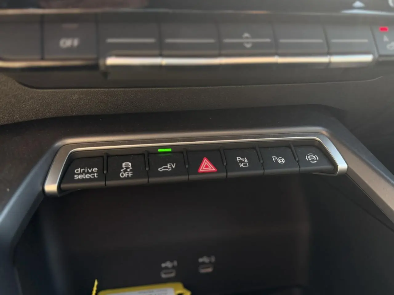 Gros plan sur la rangée de boutons de commande du tableau de bord de l’Audi A3 Sportback noir, avec éclairage vert sur le mode EV.