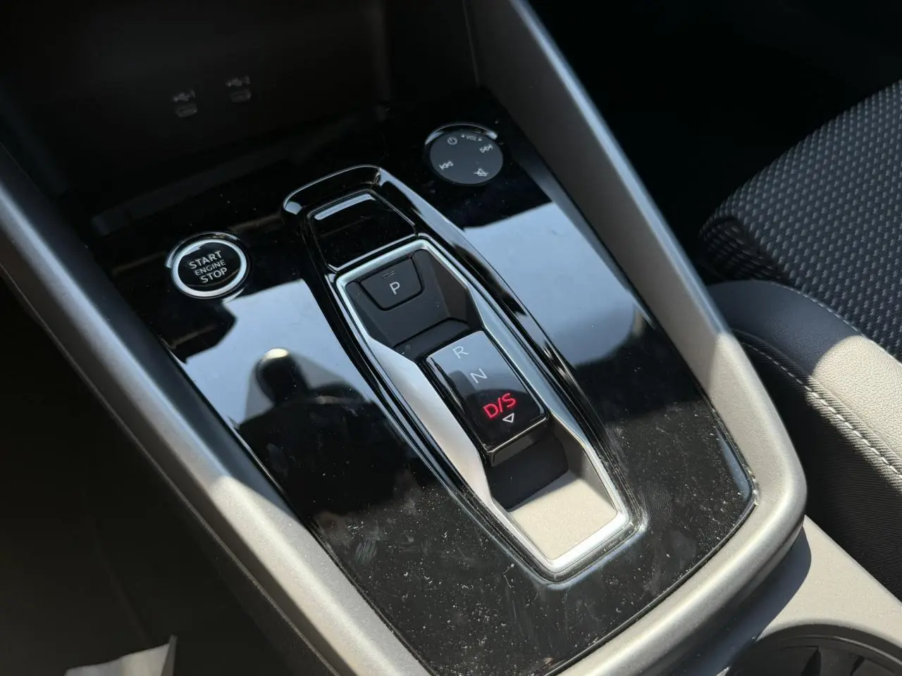 Gros plan sur la console centrale noire brillante de l'Audi A3 Sportback 2025 avec levier de vitesses automatique et bouton start/stop.