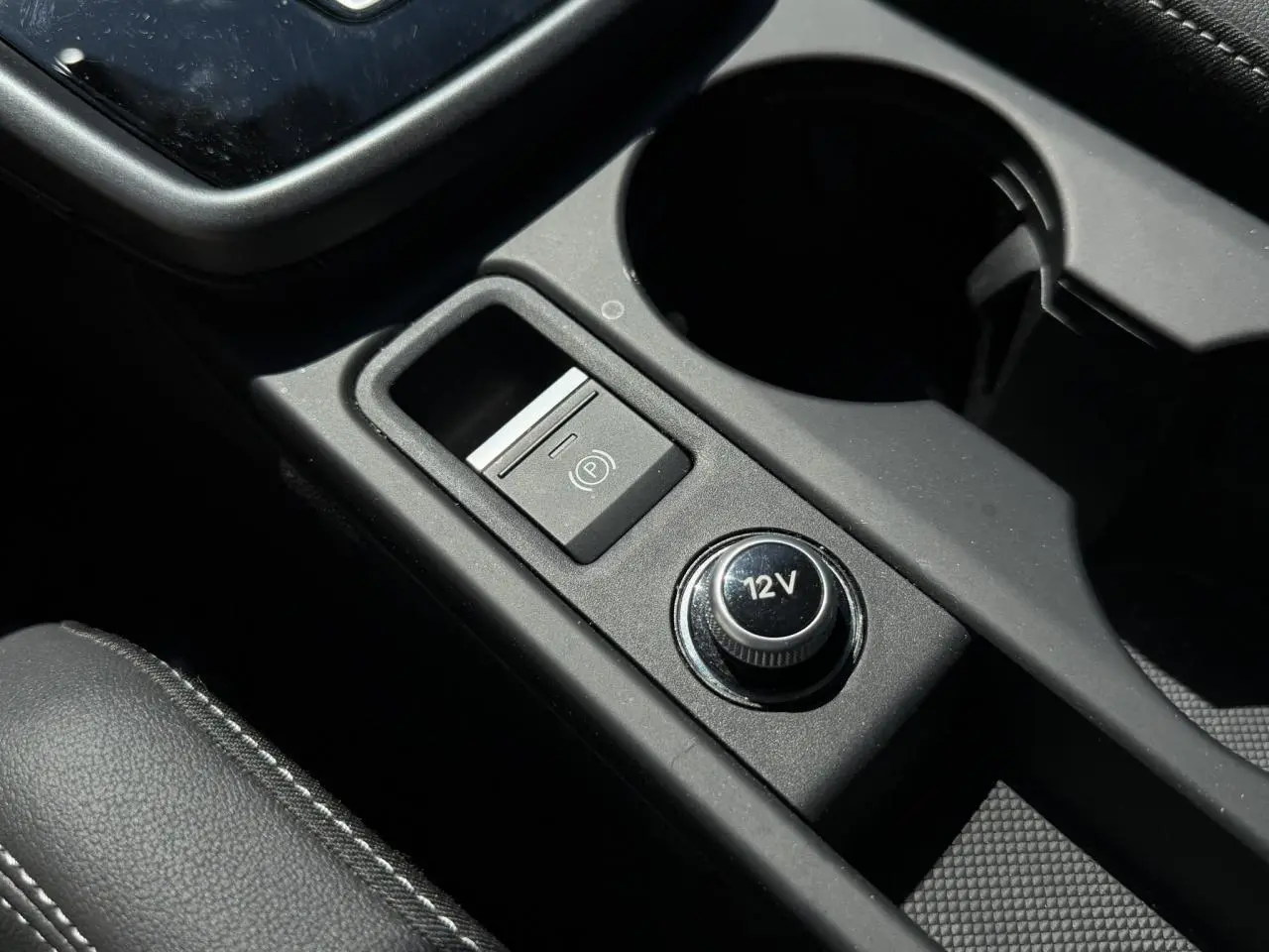 Gros plan sur la console centrale noire de l’Audi A3 Sportback 2025, avec bouton 12V et frein à main électrique.