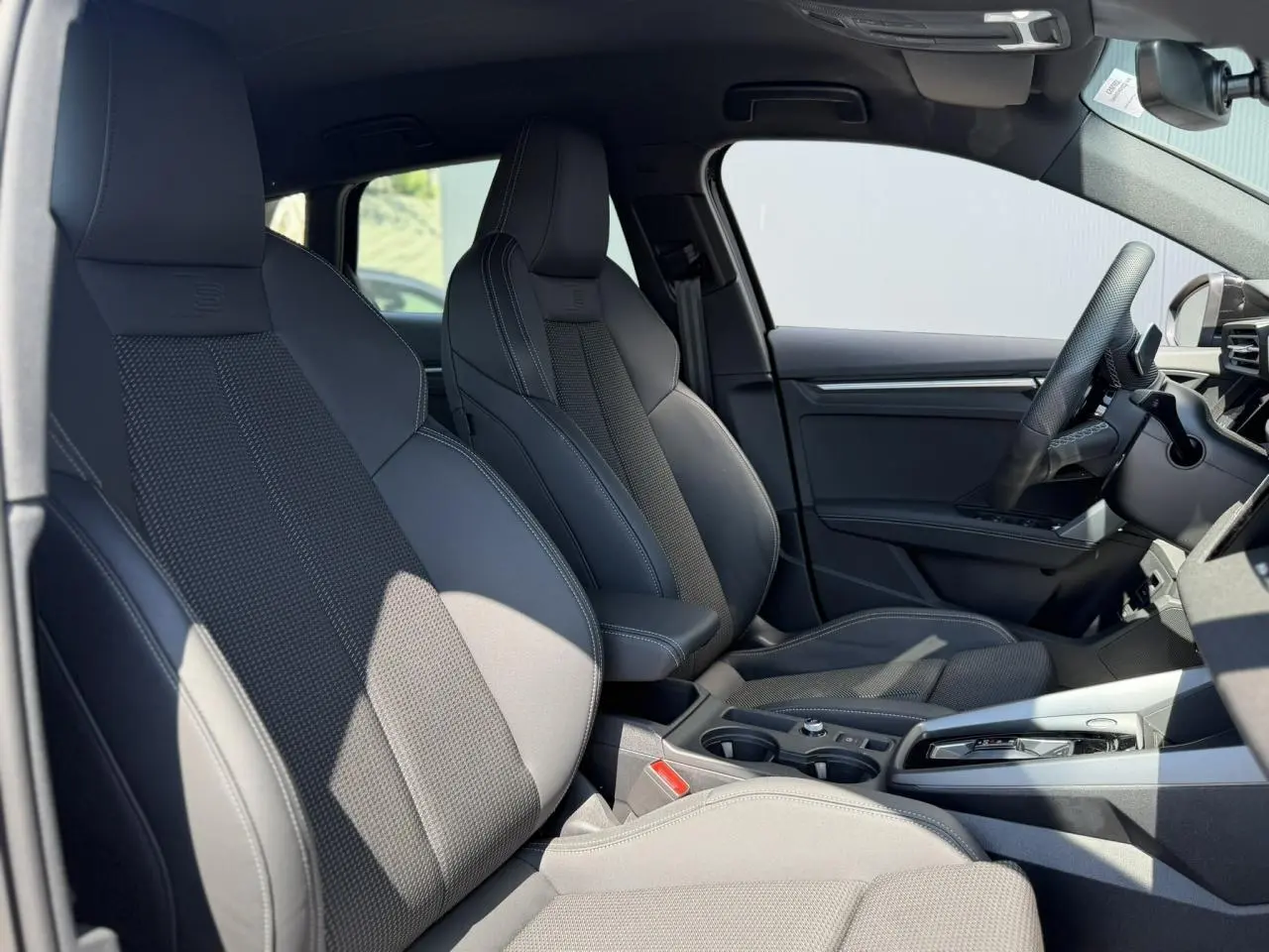 Vue intérieure côté gauche de l'Audi A3 Sportback 2025 avec sièges sport noirs et console centrale élégante.