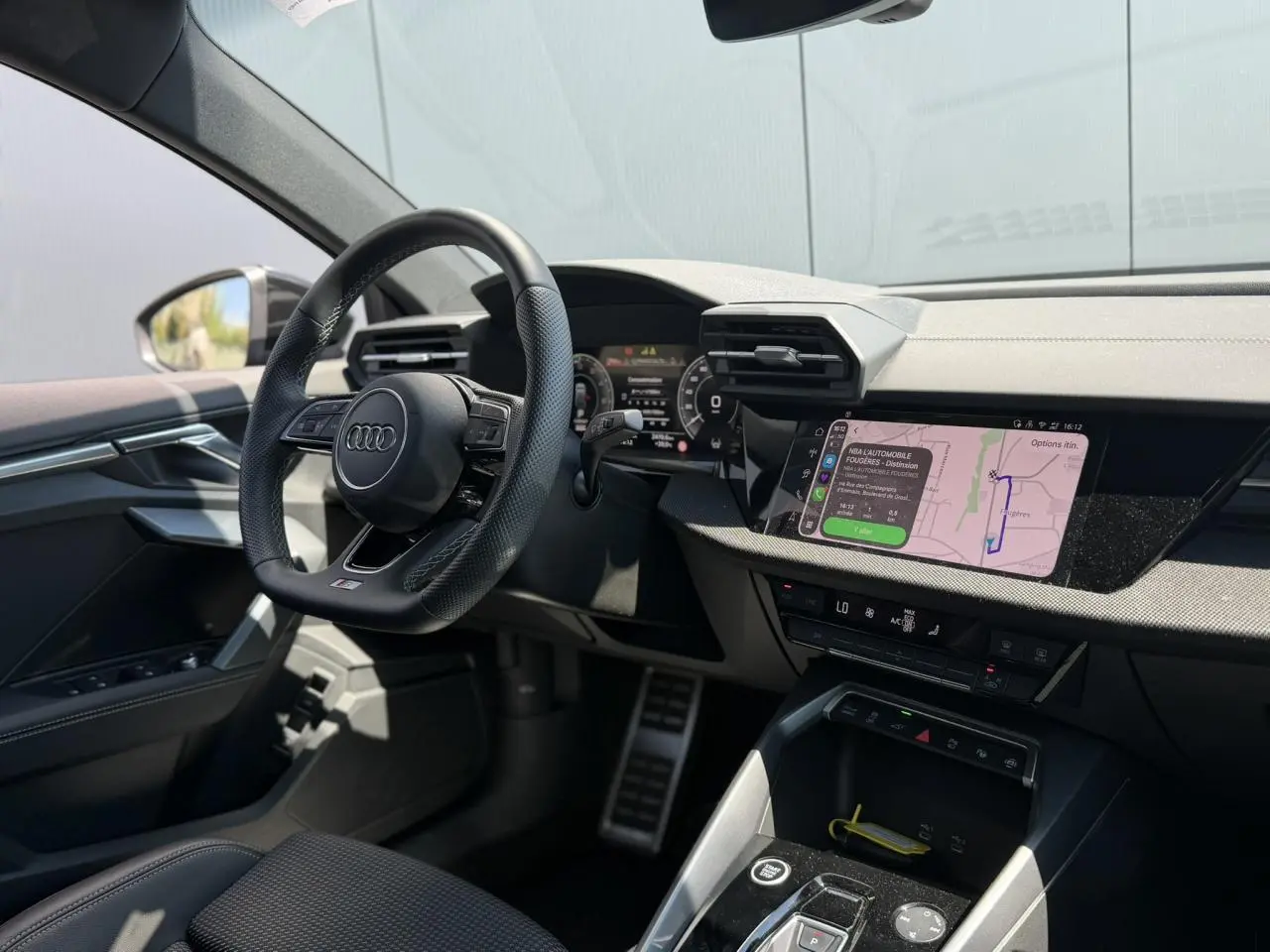 Vue intérieure côté conducteur de l'Audi A3 Sportback 2025, volant cuir perforé et écran tactile de navigation allumé.