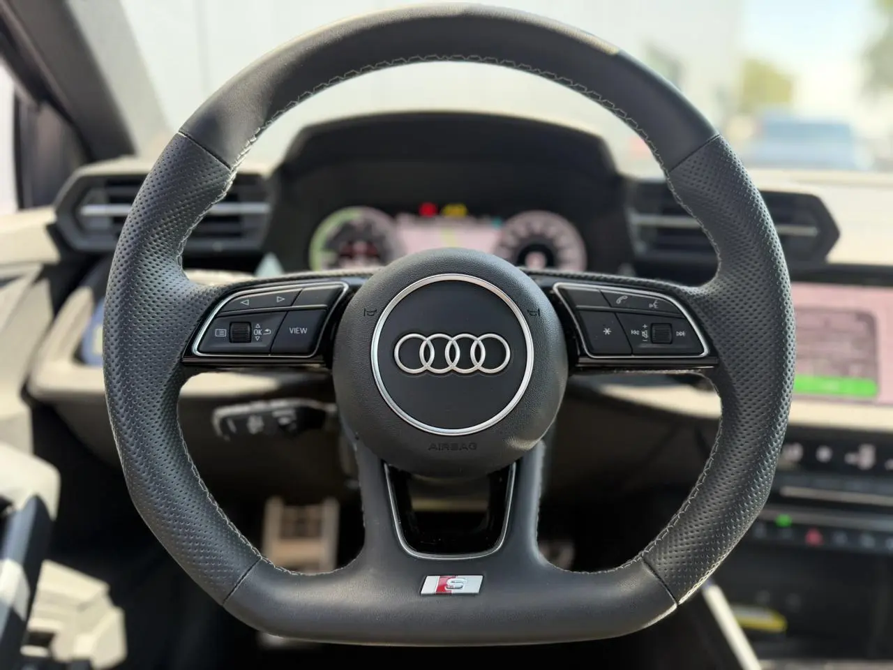 Gros plan sur le volant sport en cuir perforé avec logo Audi et badge S, intérieur moderne et lumineux.