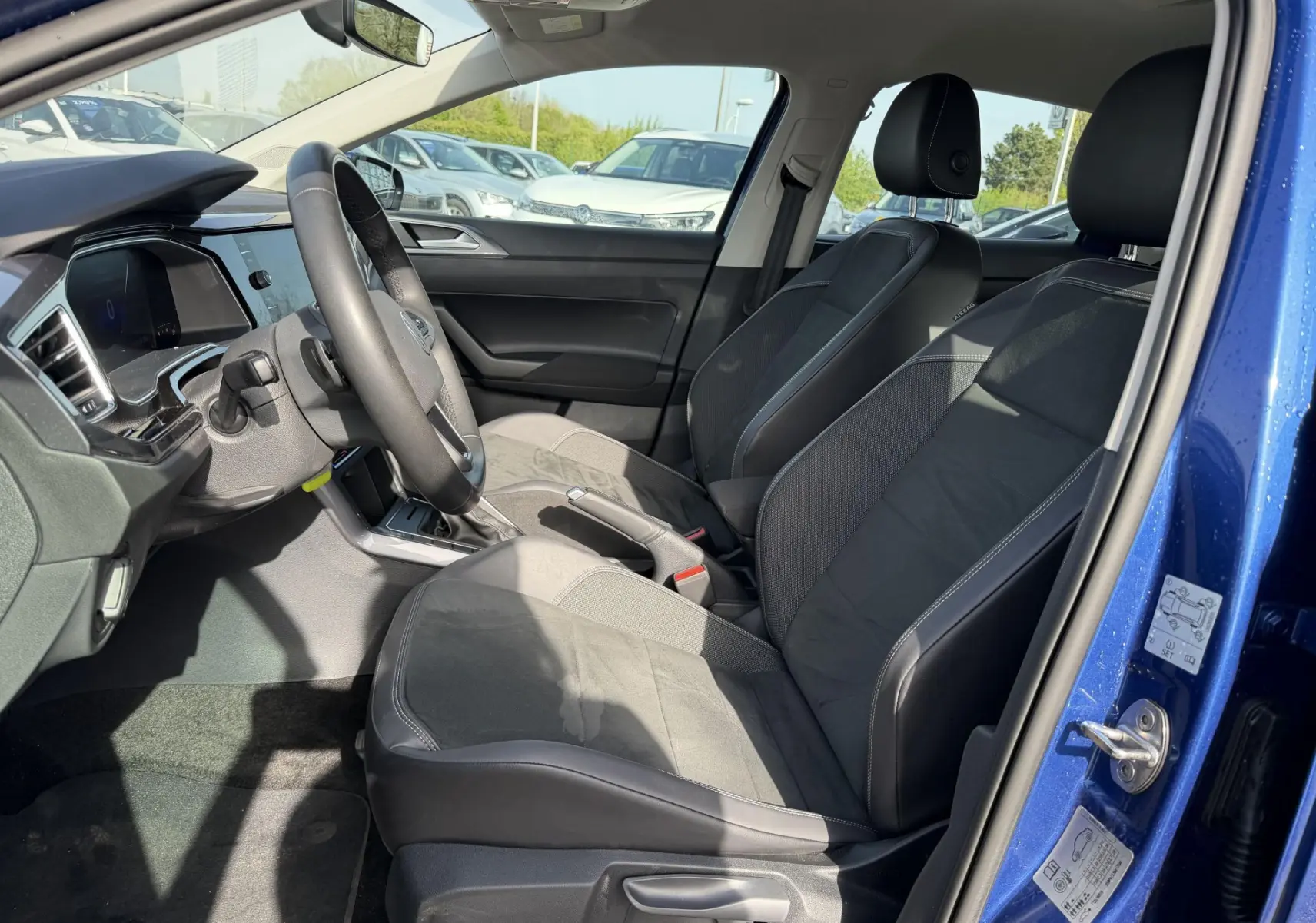 Vue intérieure côté conducteur de la Volkswagen Polo bleue 2025, sièges sport noirs et volant multifonctions cuir.
