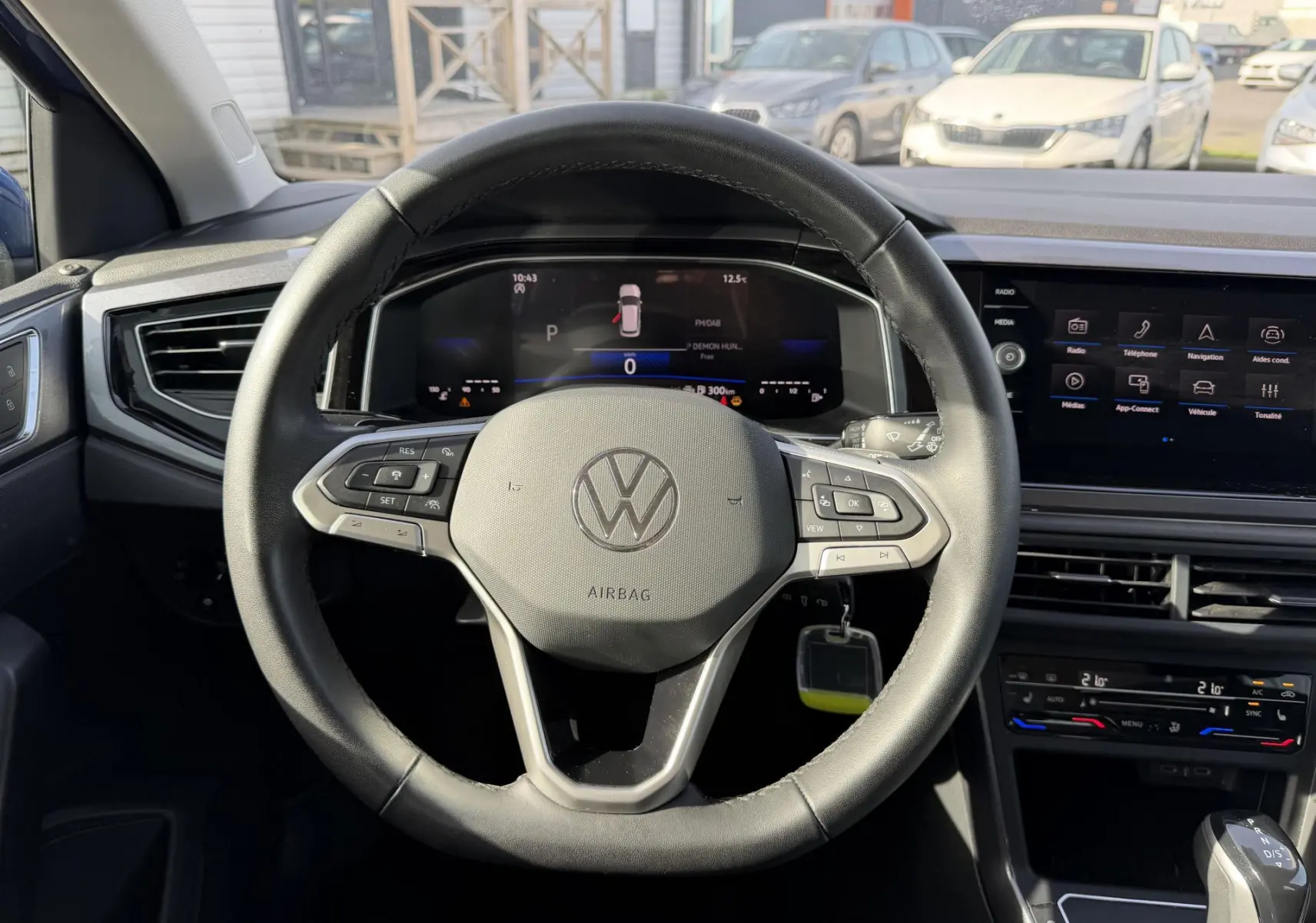 Vue intérieure centrée sur le volant cuir multifonctions d'une Volkswagen Polo bleue avec tableau de bord digital et écran tactile.