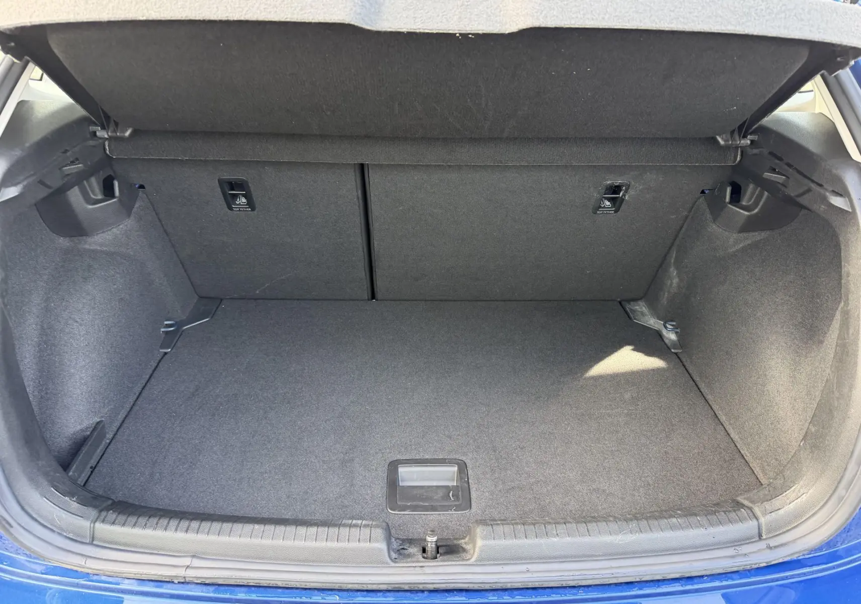 Coffre ouvert vu de l'arrière d'une Volkswagen Polo bleue, montrant un espace de chargement propre et spacieux.