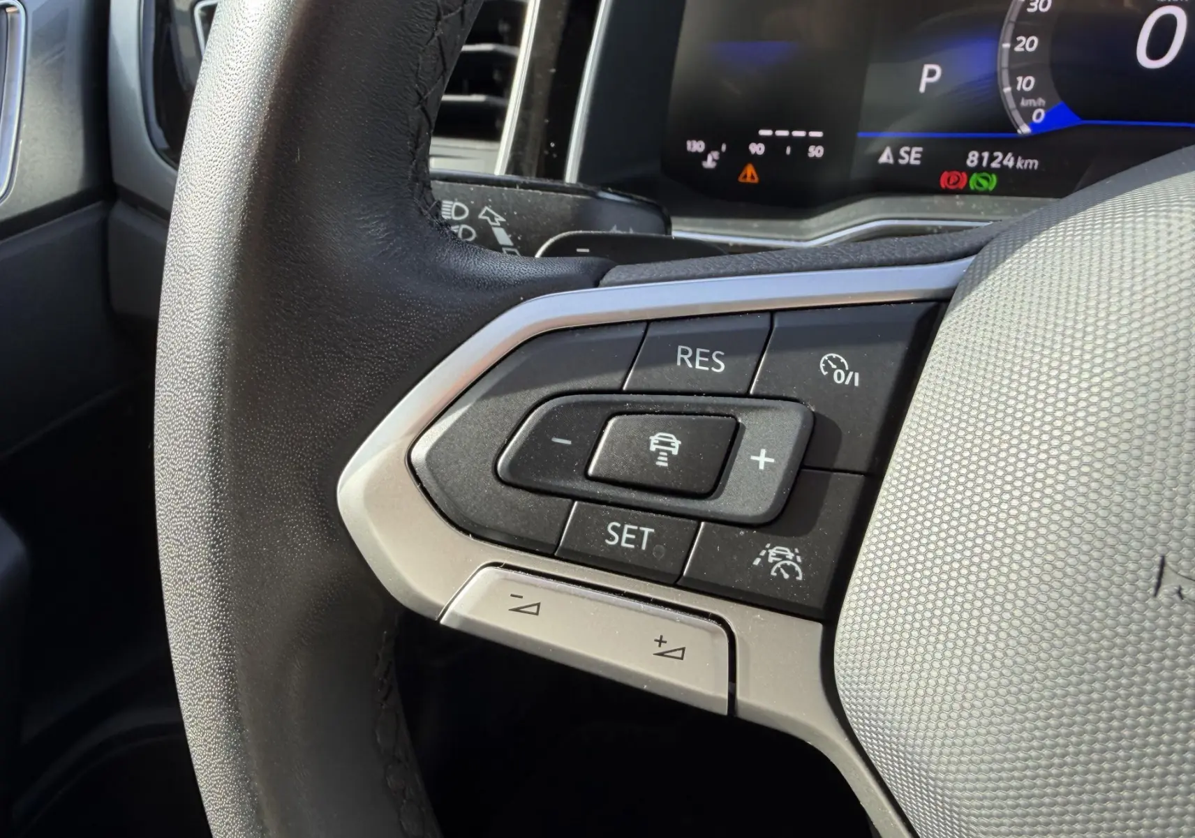 Gros plan sur le volant cuir multifonctions côté gauche de la Volkswagen Polo bleue avec commandes de régulateur adaptatif.
