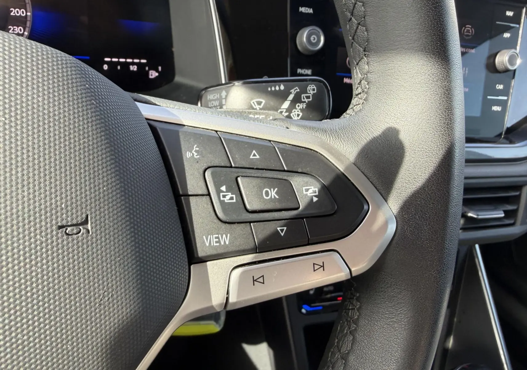 Gros plan sur le volant cuir noir de la Volkswagen Polo 2025, avec commandes multifonctions et écran tactile en arrière-plan.