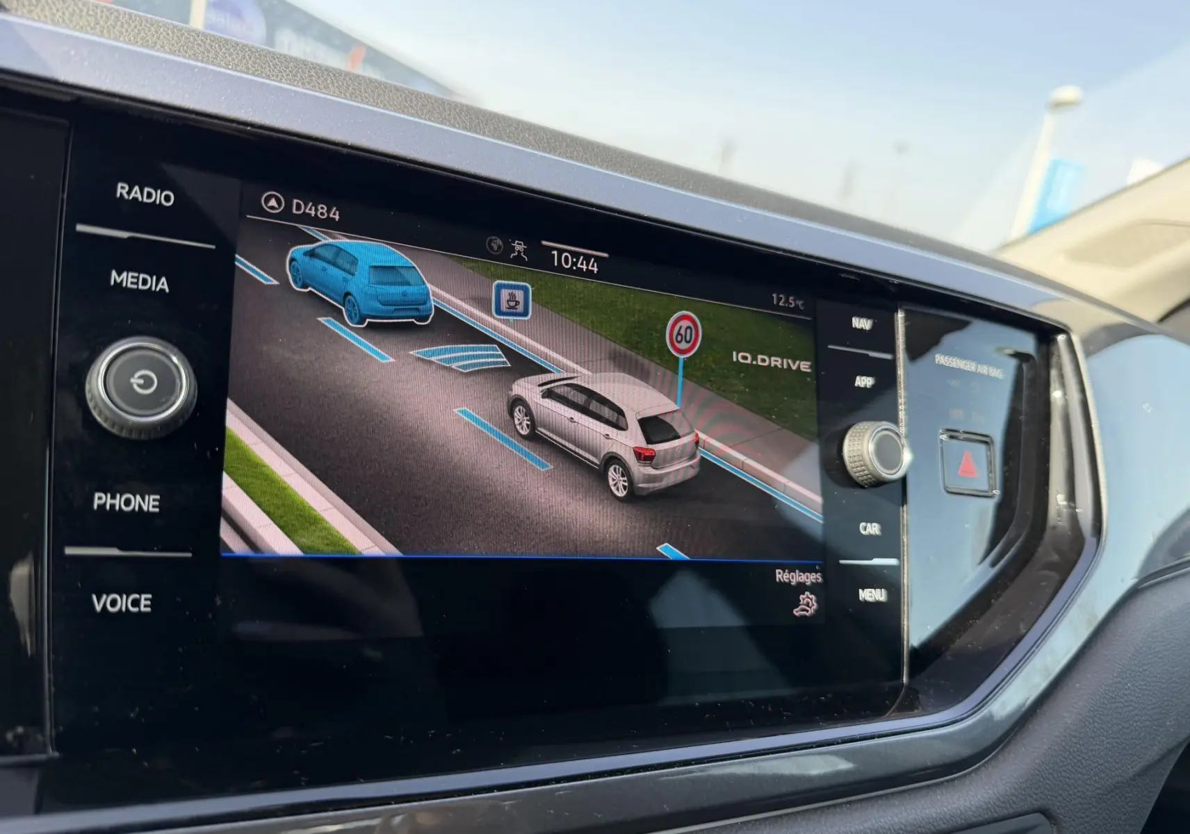 Écran tactile du tableau de bord montrant la caméra de recul avec vue arrière d'une Volkswagen Polo bleue en stationnement.