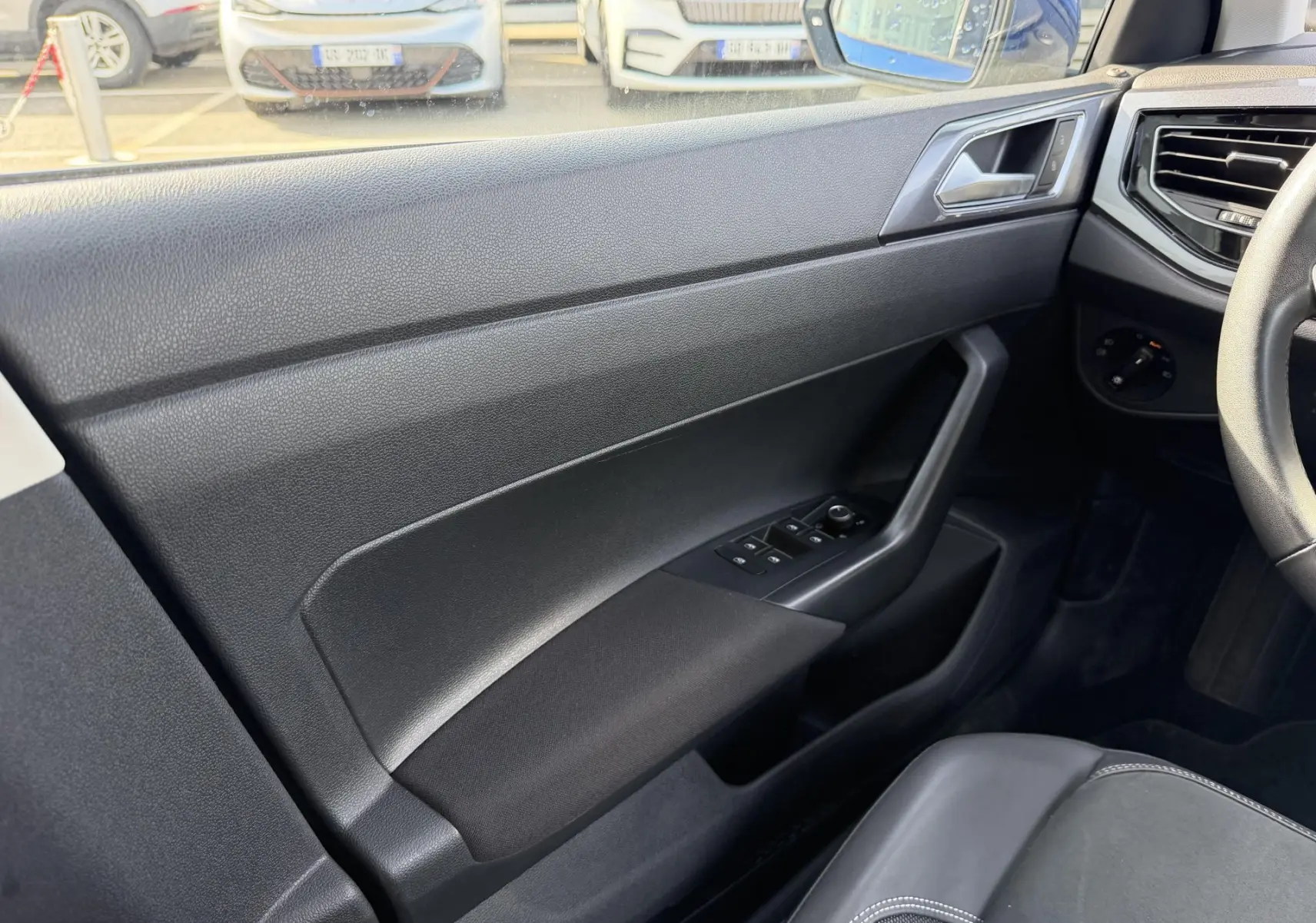 Vue intérieure côté conducteur de la Volkswagen Polo 2025 bleu récif, avec panneau de porte noir et commandes électriques.