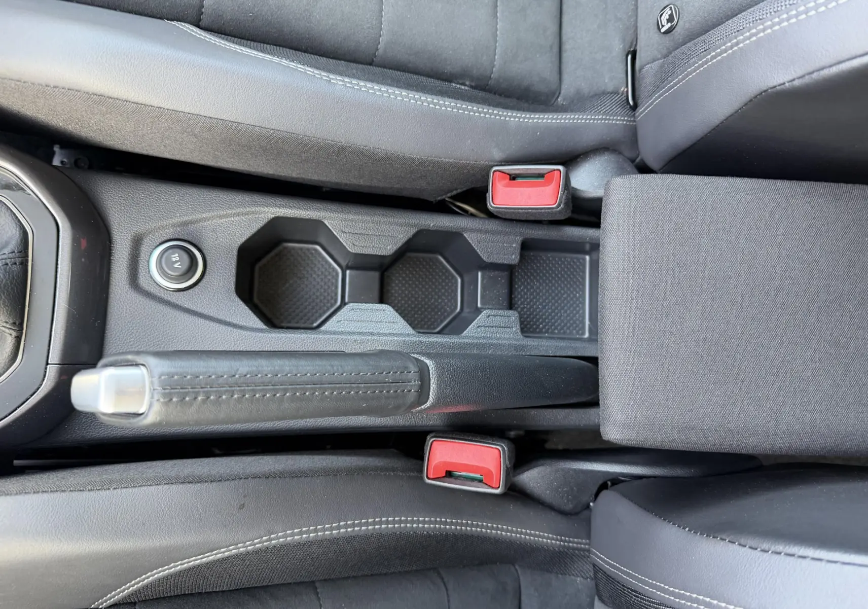 Vue plongeante sur la console centrale noire de la Volkswagen Polo avec frein à main manuel et sièges tissu gris.