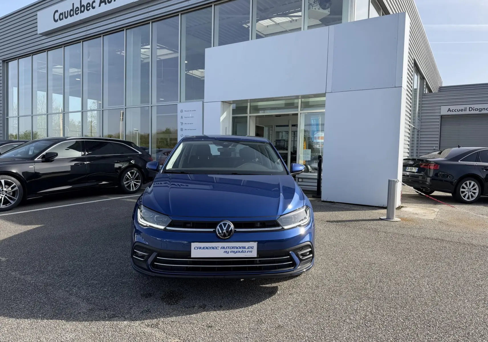 Vue avant d'une Volkswagen Polo bleu récif métallisé garée devant un showroom avec calandre et logo VW visibles.