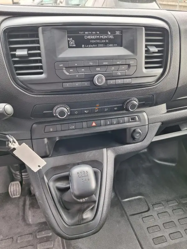 Vue rapprochée de la console centrale noire de l’Opel Vivaro 2025 avec boîte manuelle et écran radio affichant une station FM.